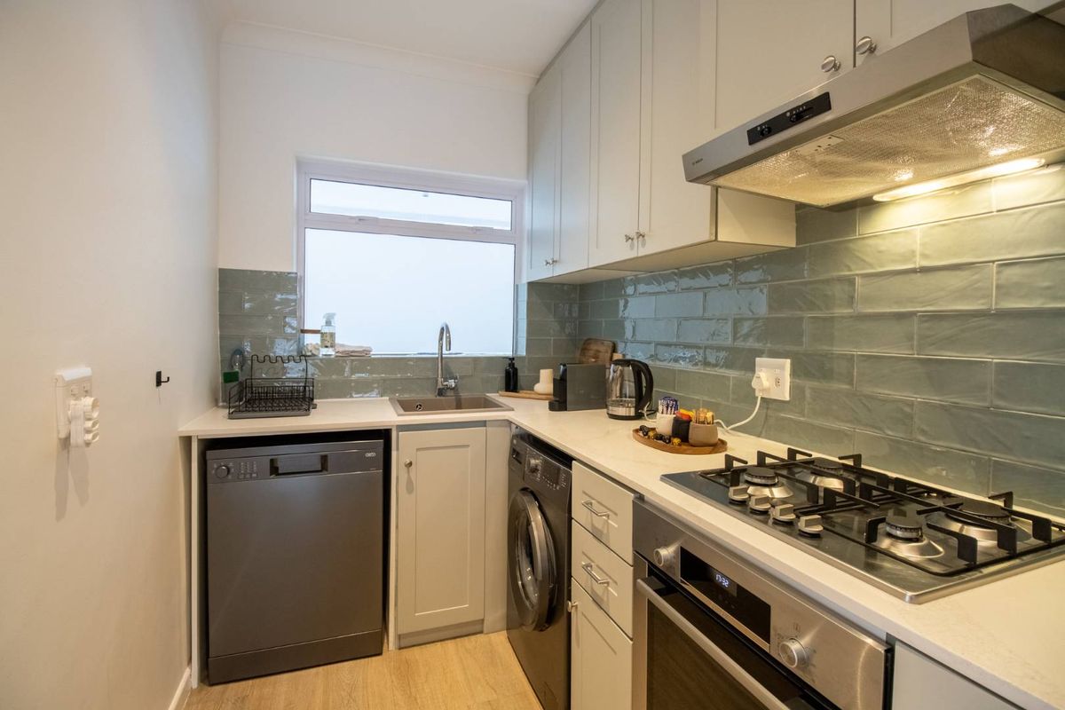 A compact, modern kitchen featuring light cabinetry, stone countertops, a gas hob, integrated oven, and stylish subway tile backsplash.