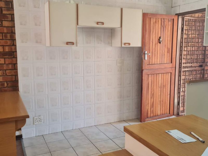 A dated kitchen area featuring tiled walls, built-in cabinetry, and exposed brickwork, offering a blank canvas for modern renovation and design updates.