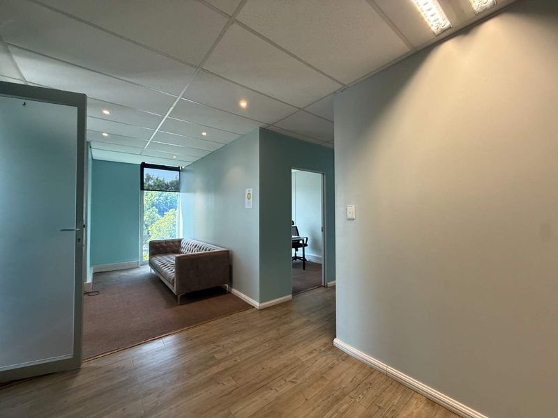 A professional office space featuring a mix of laminate and carpet flooring, suspended ceilings with recessed lighting, and a glass entrance door.