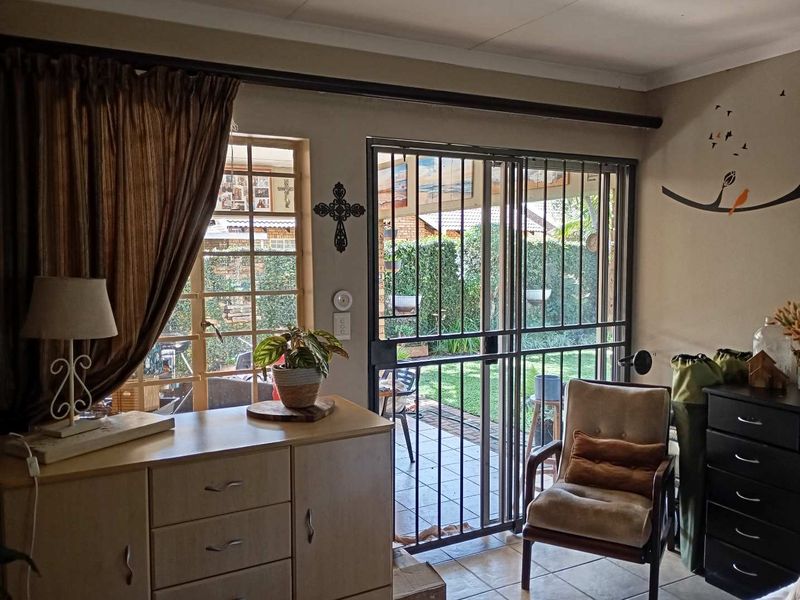 Living area featuring tiled flooring, security bars on windows, and a sliding security gate providing access to the rear patio and garden.