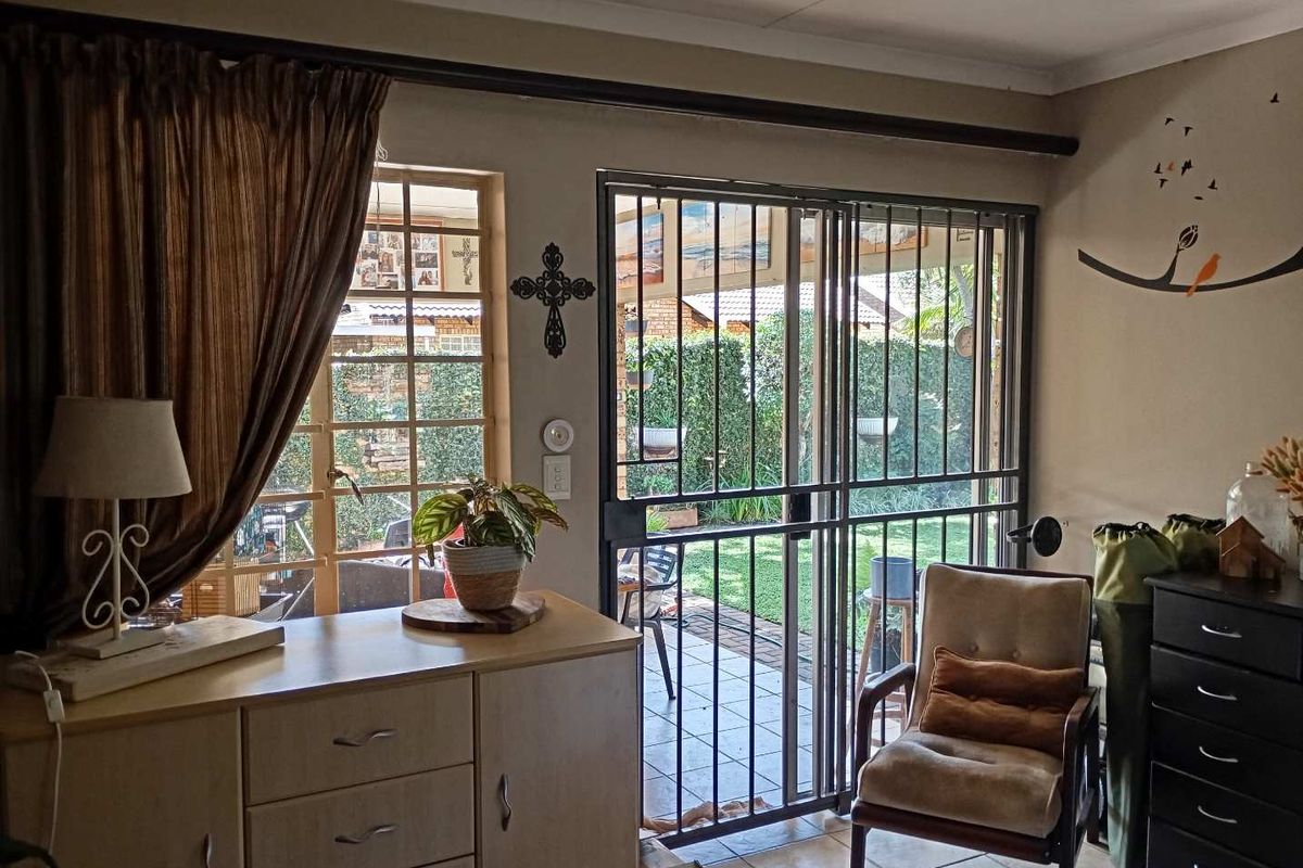 Living area featuring tiled flooring, security bars on windows, and a sliding security gate providing access to the rear patio and garden.