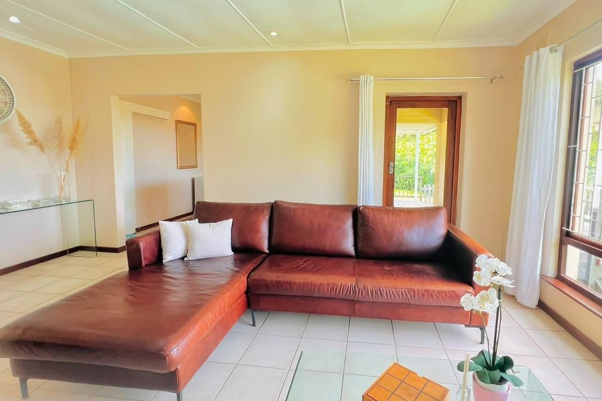 A bright living room featuring neutral tiled flooring, recessed ceiling lighting, and a timber door leading to an outdoor area.