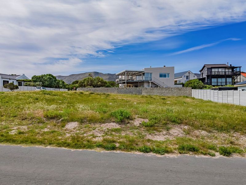 A vacant residential plot featuring road frontage and concrete boundary walls, situated in a developed neighborhood with mountain views.