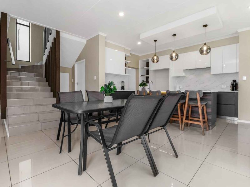 Modern open-plan living area featuring a sleek kitchen with island, contemporary cabinetry, tiled floors, and a staircase leading to the upper level.
