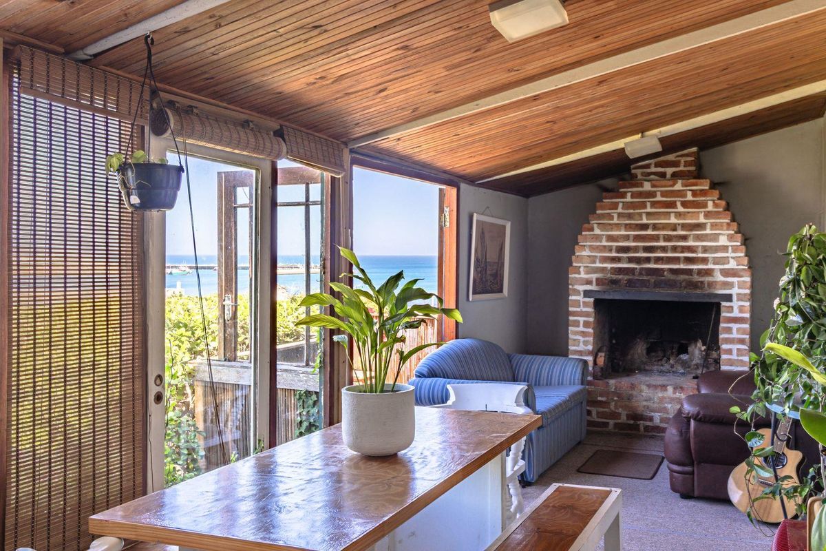 A sunroom featuring a brick fireplace, timber-clad ceiling, and large glass doors opening to a coastal view.