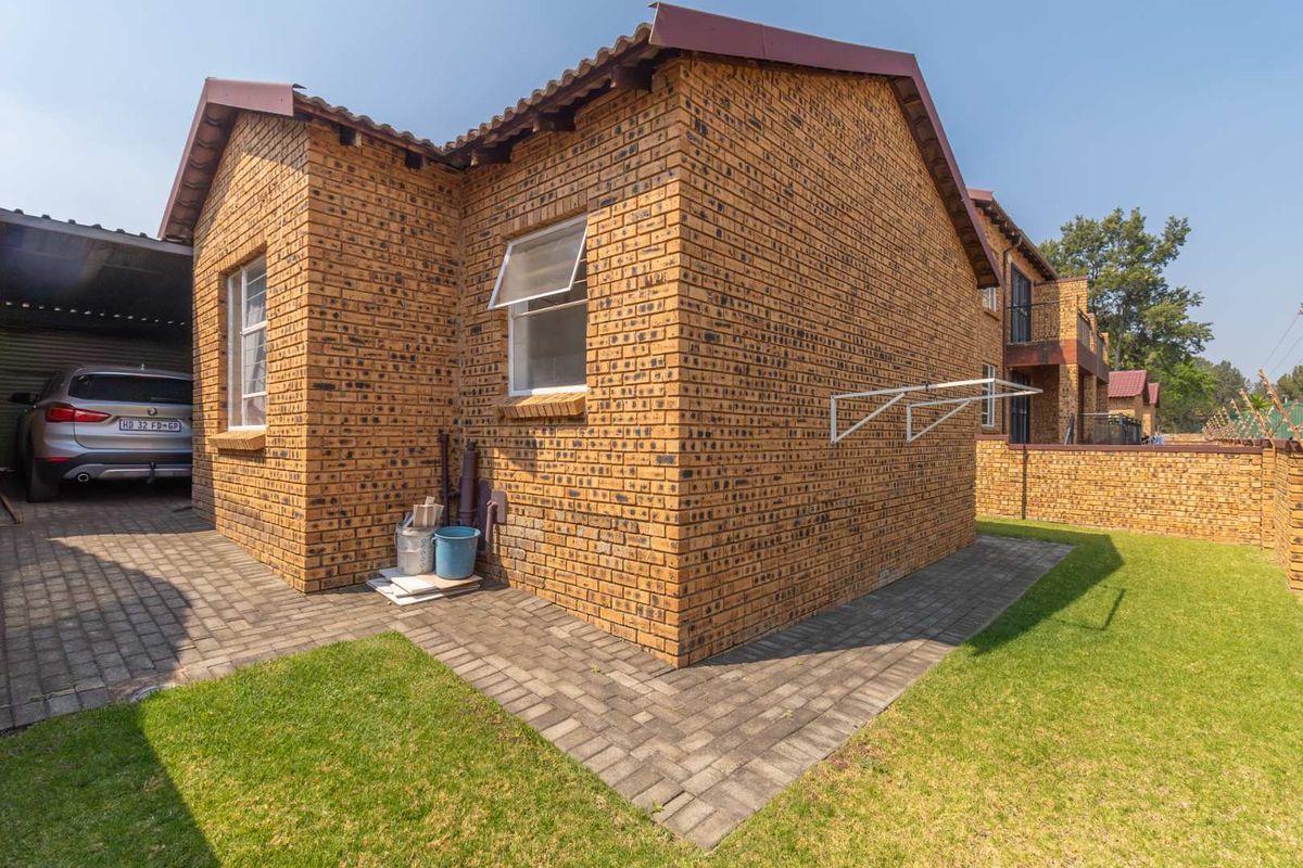 Side view of the townhouse featuring face-brick exterior, paved walkway, small lawn area, and a covered carport structure.