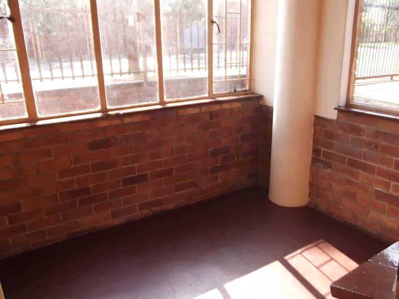 An enclosed patio area featuring exposed brick walls, large steel-framed windows, and a painted concrete floor, offering a versatile space for potential renovation.