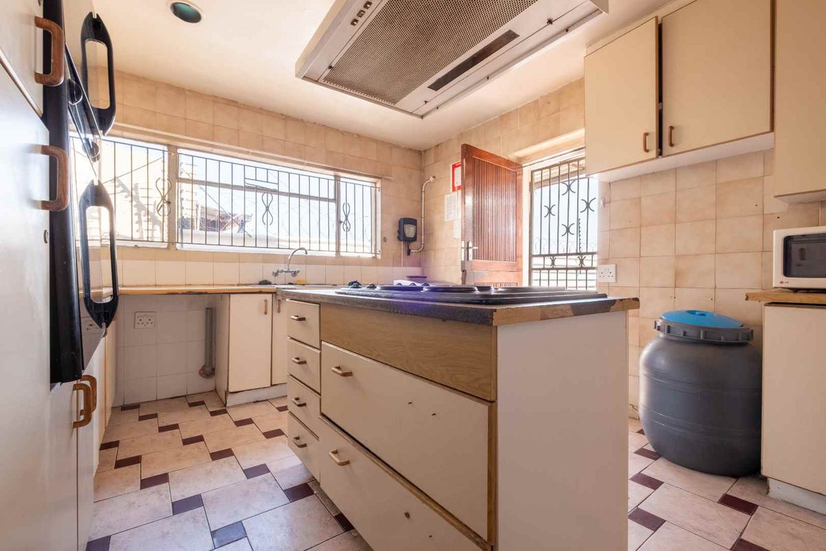 A dated kitchen featuring a central island, built-in cabinetry, an integrated extractor fan, and tiled flooring with security bars on the windows.