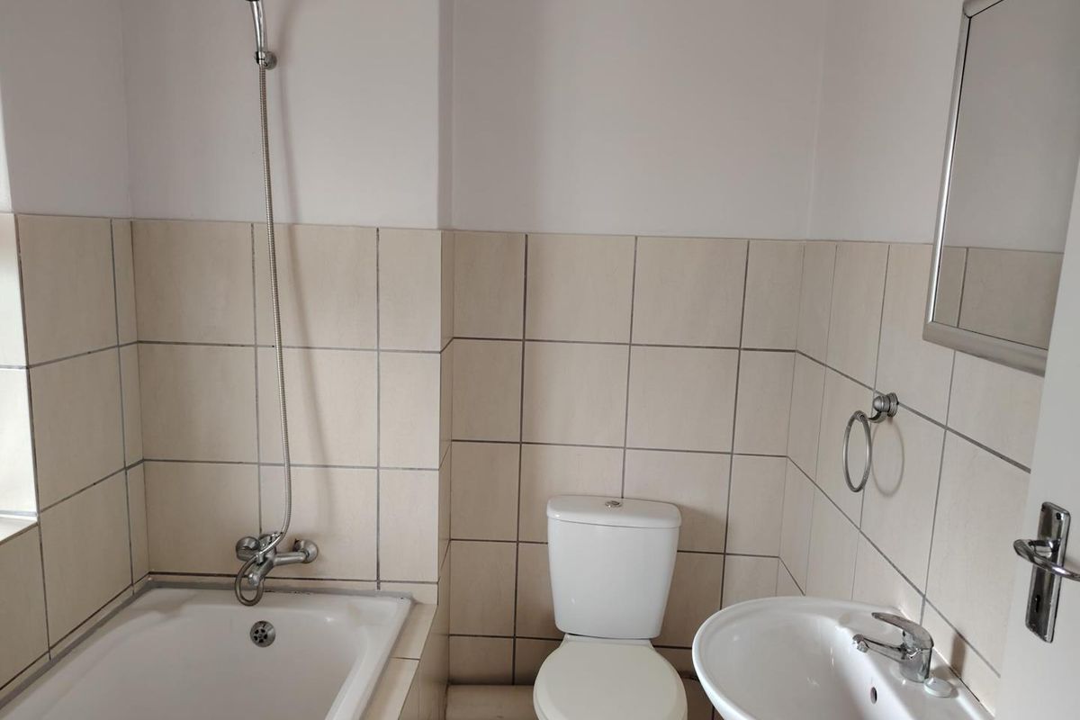 A functional bathroom featuring a bathtub with handheld shower, pedestal sink, and toilet, finished with neutral wall tiling.
