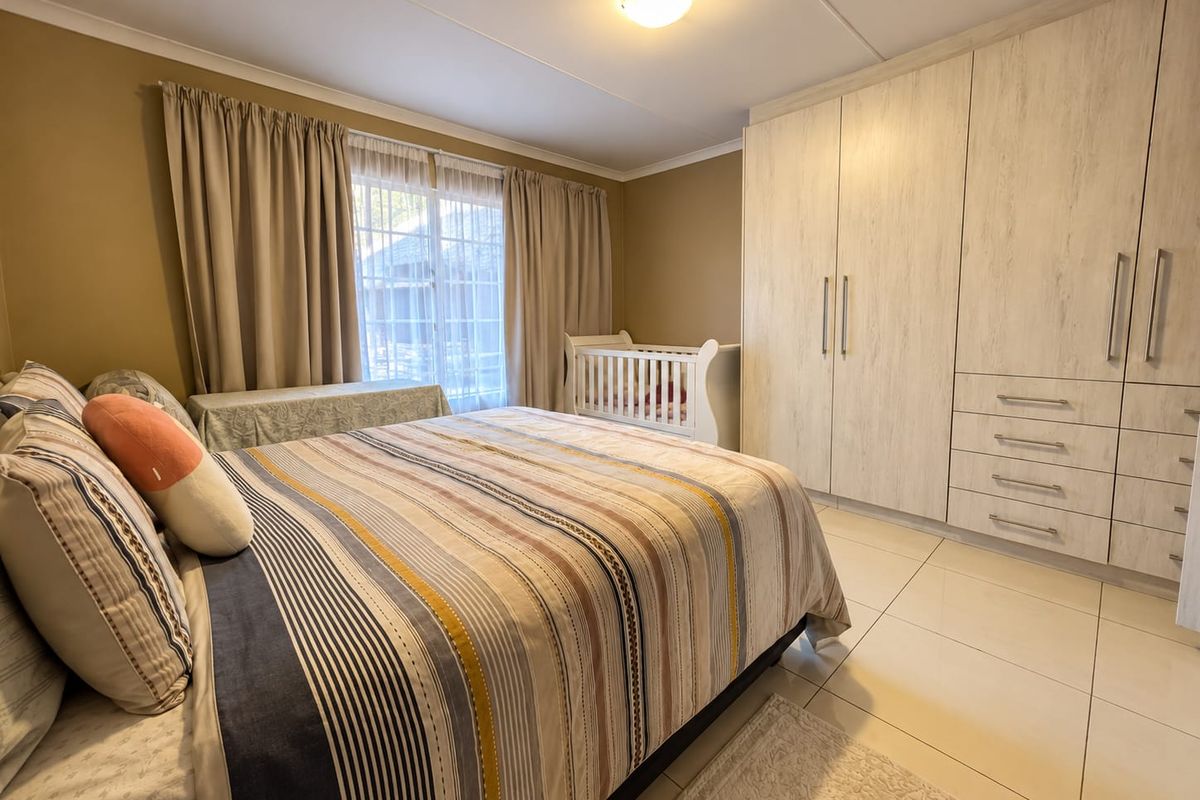 A well-maintained bedroom featuring neutral tiled flooring, ample built-in cupboard storage, and a sliding glass door providing natural light.
