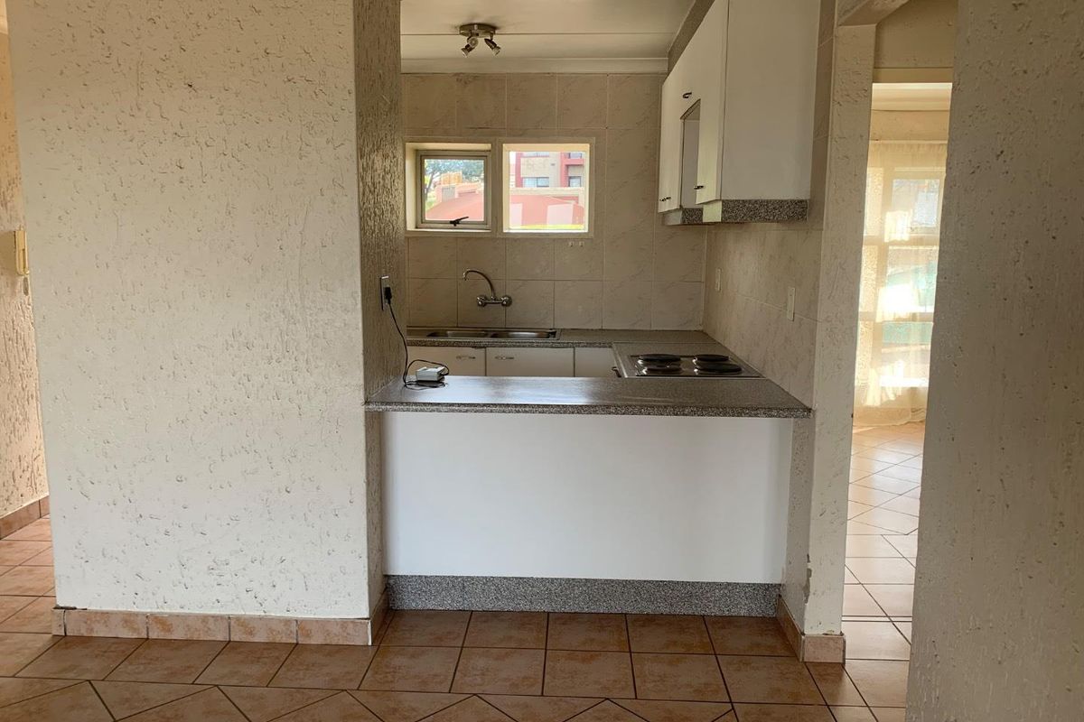 A compact kitchen featuring built-in cabinetry, granite countertops, an electric hob, and tiled flooring, offering a functional layout ready for modernization.