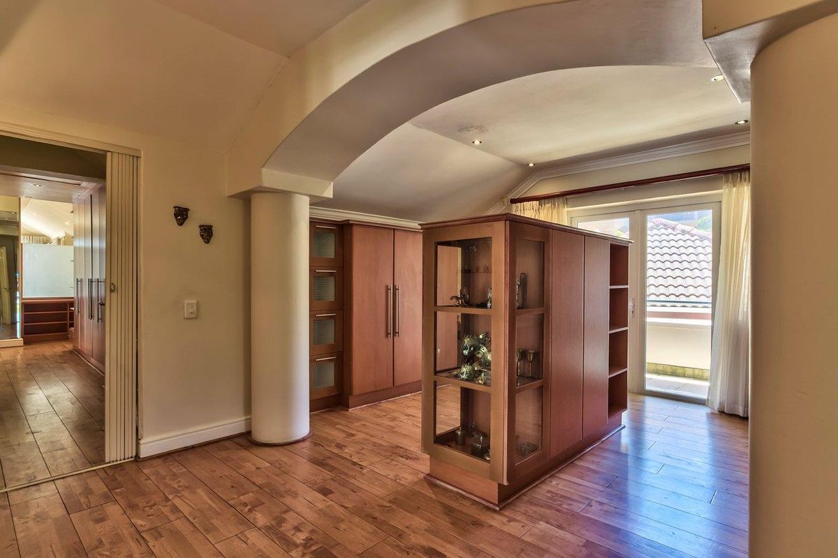 Spacious bedroom featuring warm laminate flooring, built-in wooden cabinetry, an architectural archway, and direct access to a balcony through sliding glass doors.