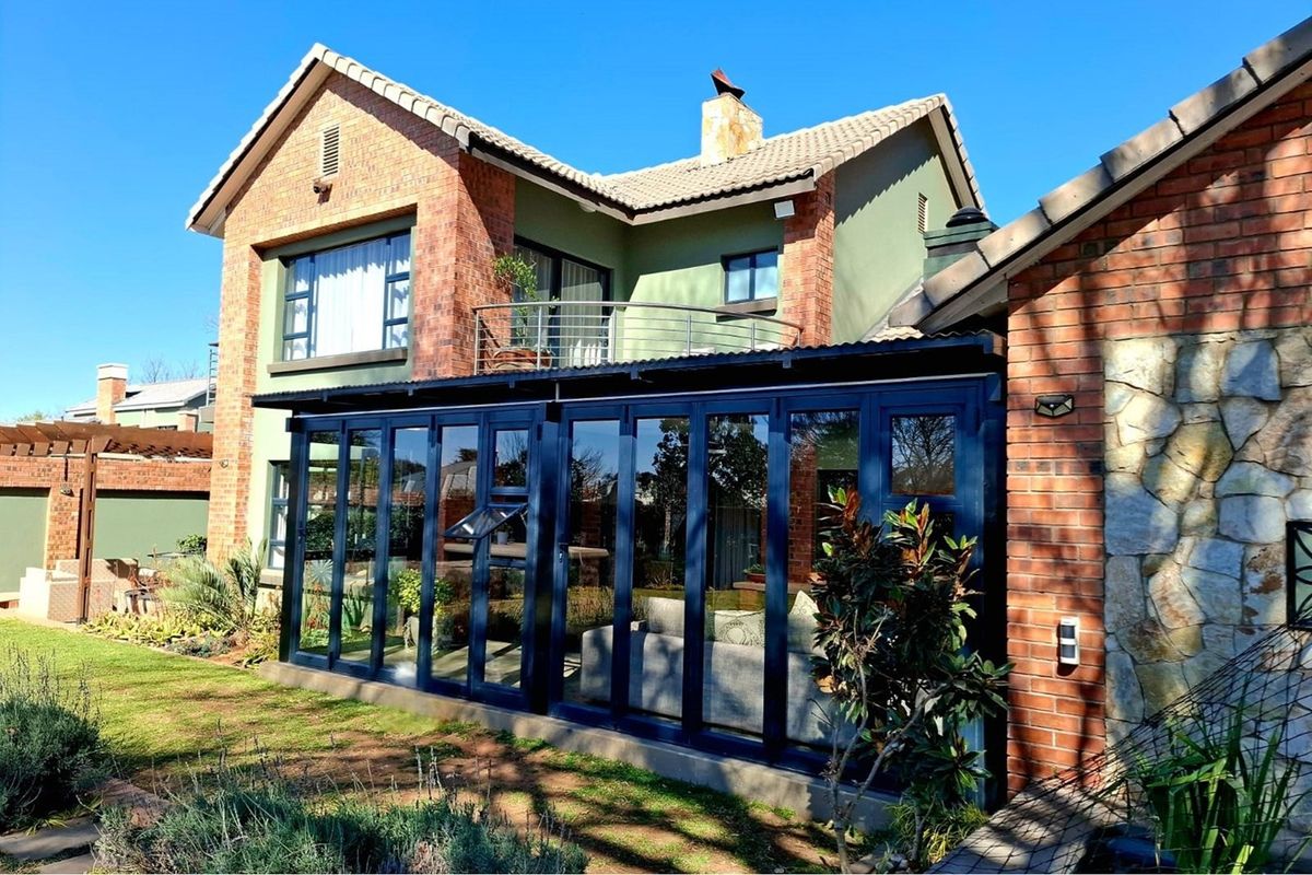 Rear view of a double-storey brick home featuring a modern enclosed patio with dark aluminium stacker doors and an upper-level balcony.