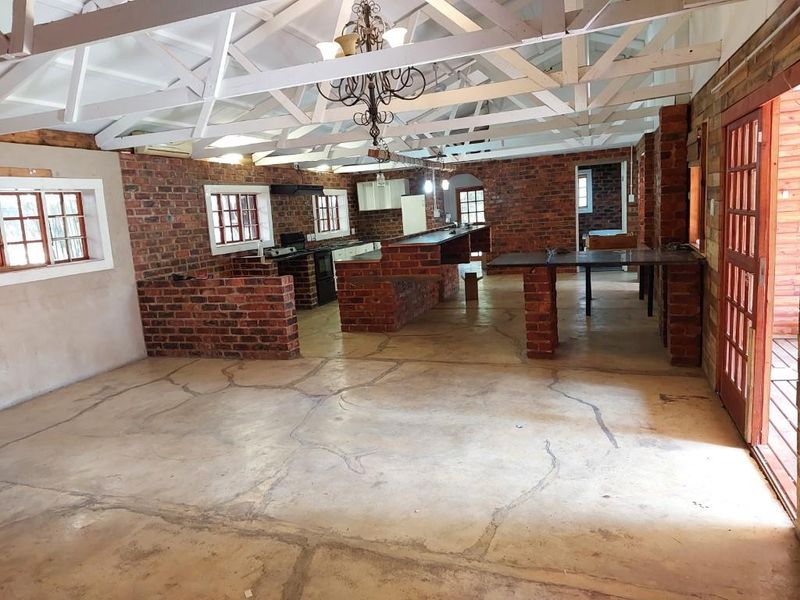 Spacious open-plan living and kitchen area featuring exposed timber roof trusses, rustic brick walls, and concrete flooring with a built-in brick island.