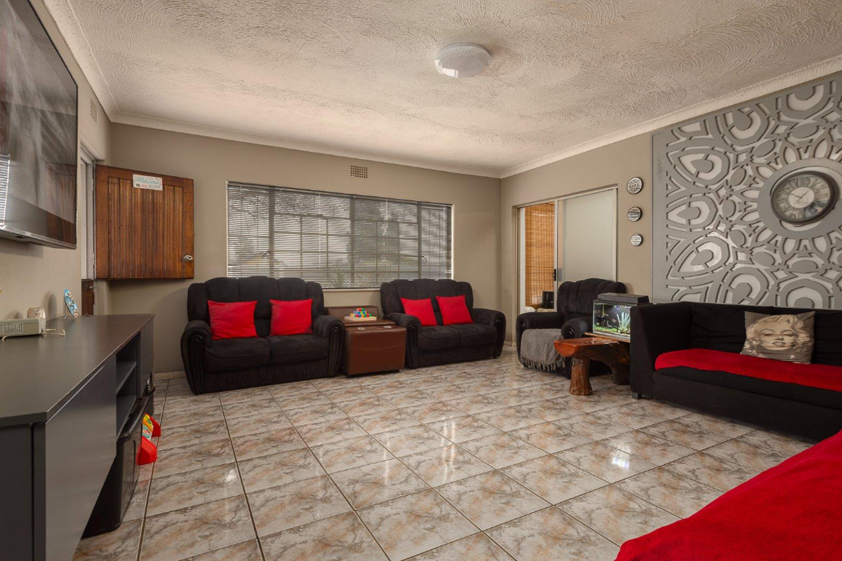 Spacious living room featuring tiled flooring, textured ceilings, and large windows providing natural light, with direct access to an adjoining outdoor area.