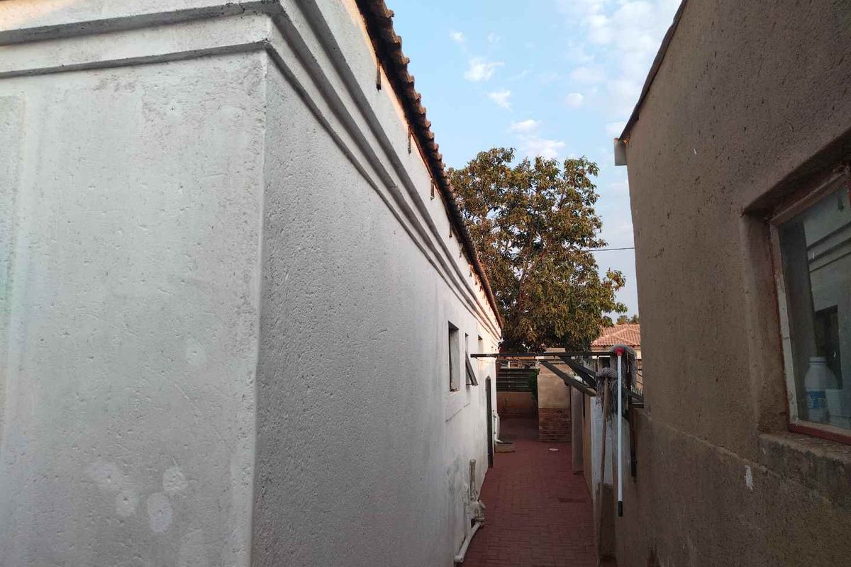 A narrow side passage between two residential structures featuring paved flooring and exterior wall access.