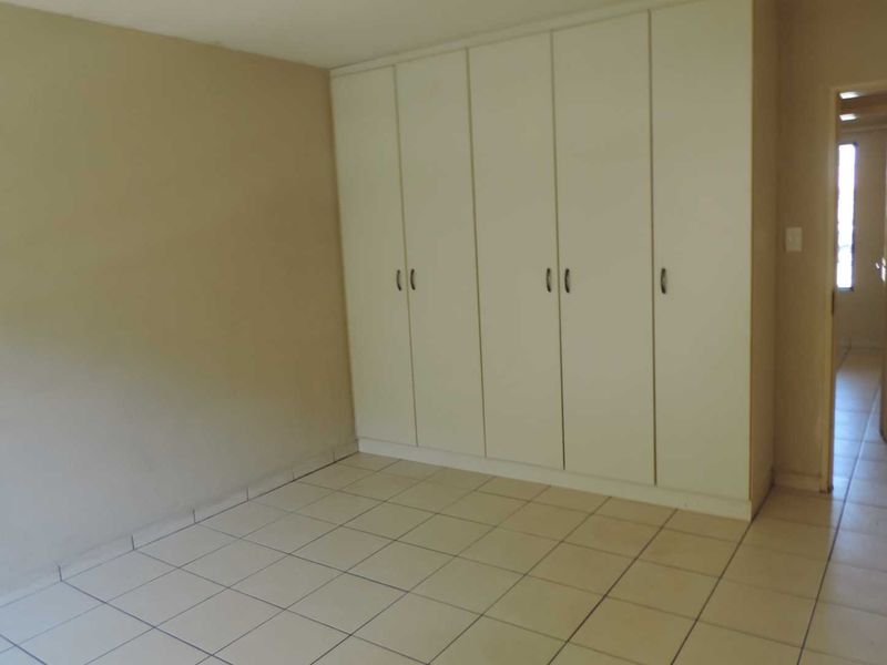 A vacant bedroom featuring neutral wall tones, tiled flooring, and ample built-in cupboard storage space.
