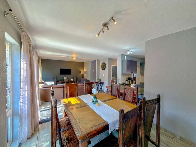 Spacious open-plan living and dining area featuring tiled flooring, modern track lighting, and a functional kitchen with granite countertops.