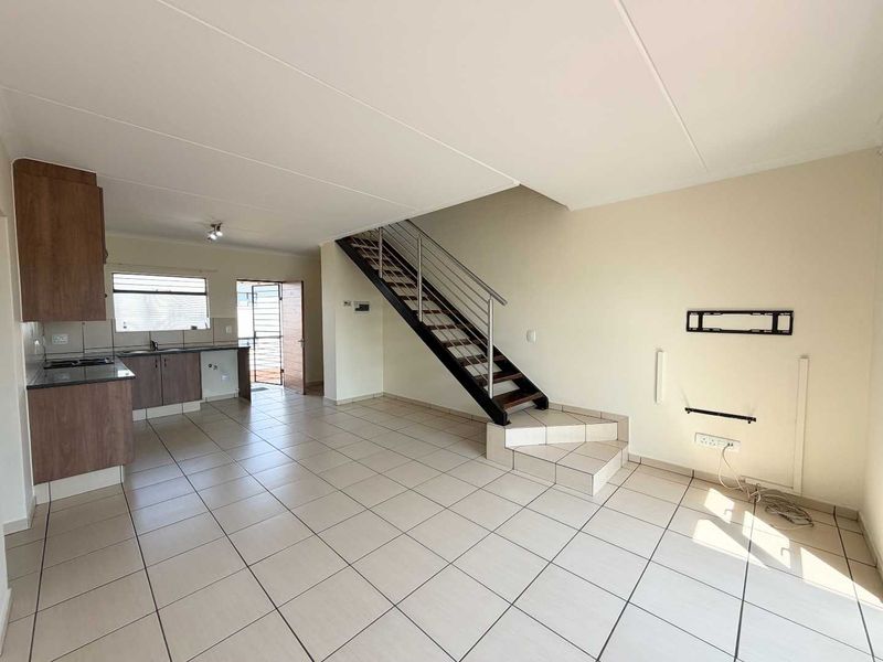 An open-plan living and kitchen area featuring tiled flooring, a modern staircase with metal railings, and functional kitchen cabinetry.