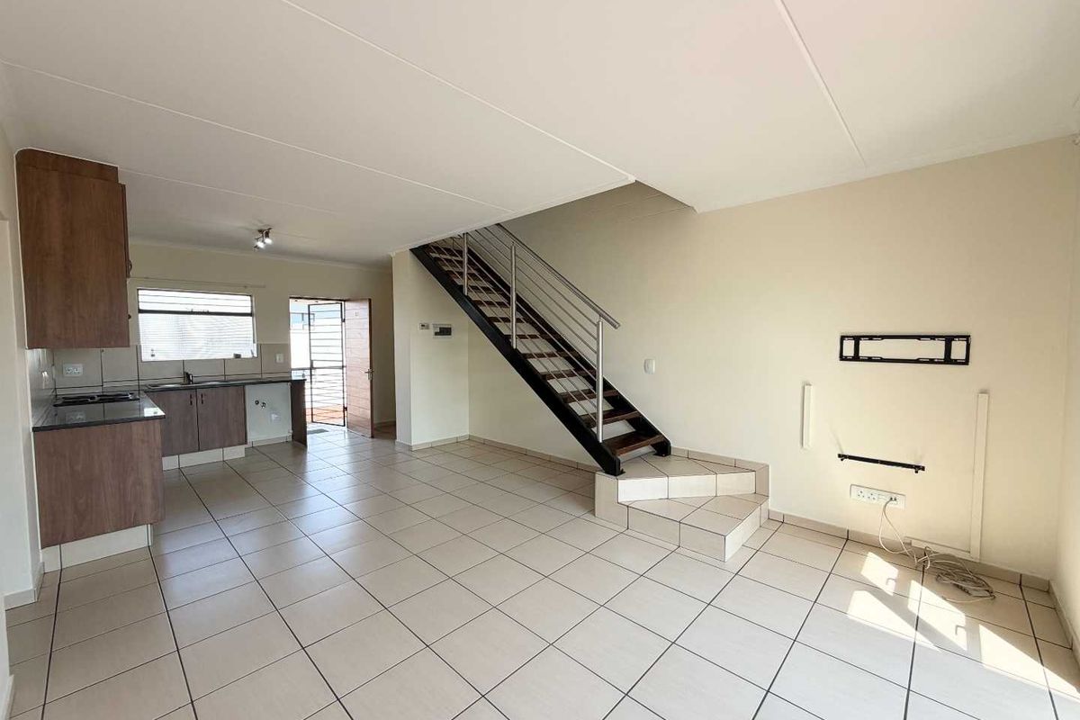 An open-plan living and kitchen area featuring tiled flooring, a modern staircase with metal railings, and functional kitchen cabinetry.