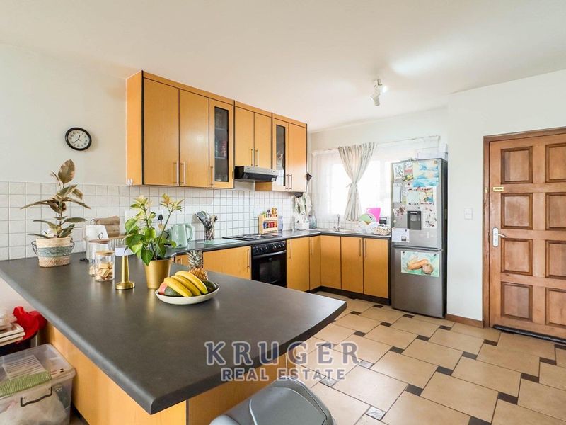 Functional kitchen featuring wooden cabinetry, tiled backsplash, built-in oven with hob, and a breakfast counter, offering a practical layout for daily cooking.