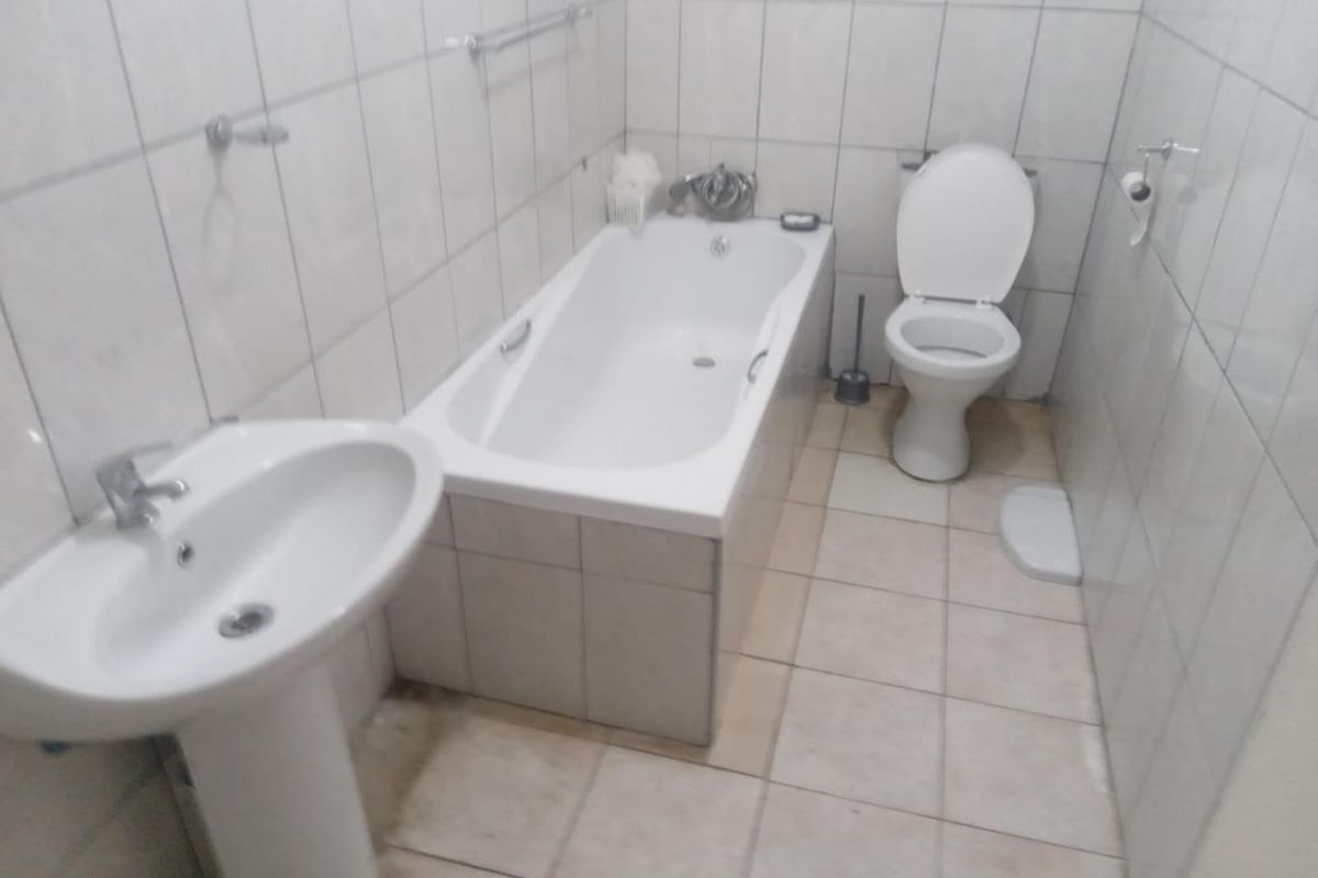 A functional bathroom featuring a pedestal basin, a standard bathtub with shower mixer, and a toilet, finished with full-height wall tiling.