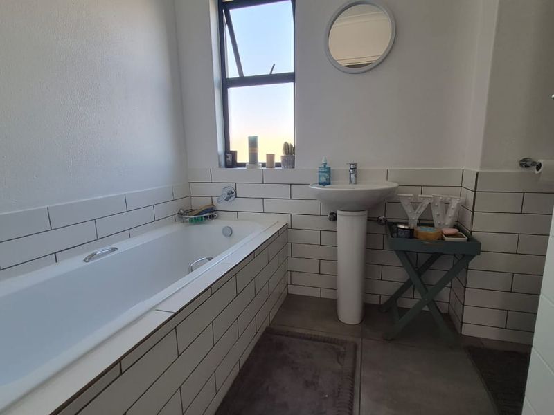 A clean, modern bathroom featuring a built-in bathtub, pedestal basin, and classic white subway wall tiles with dark grout.