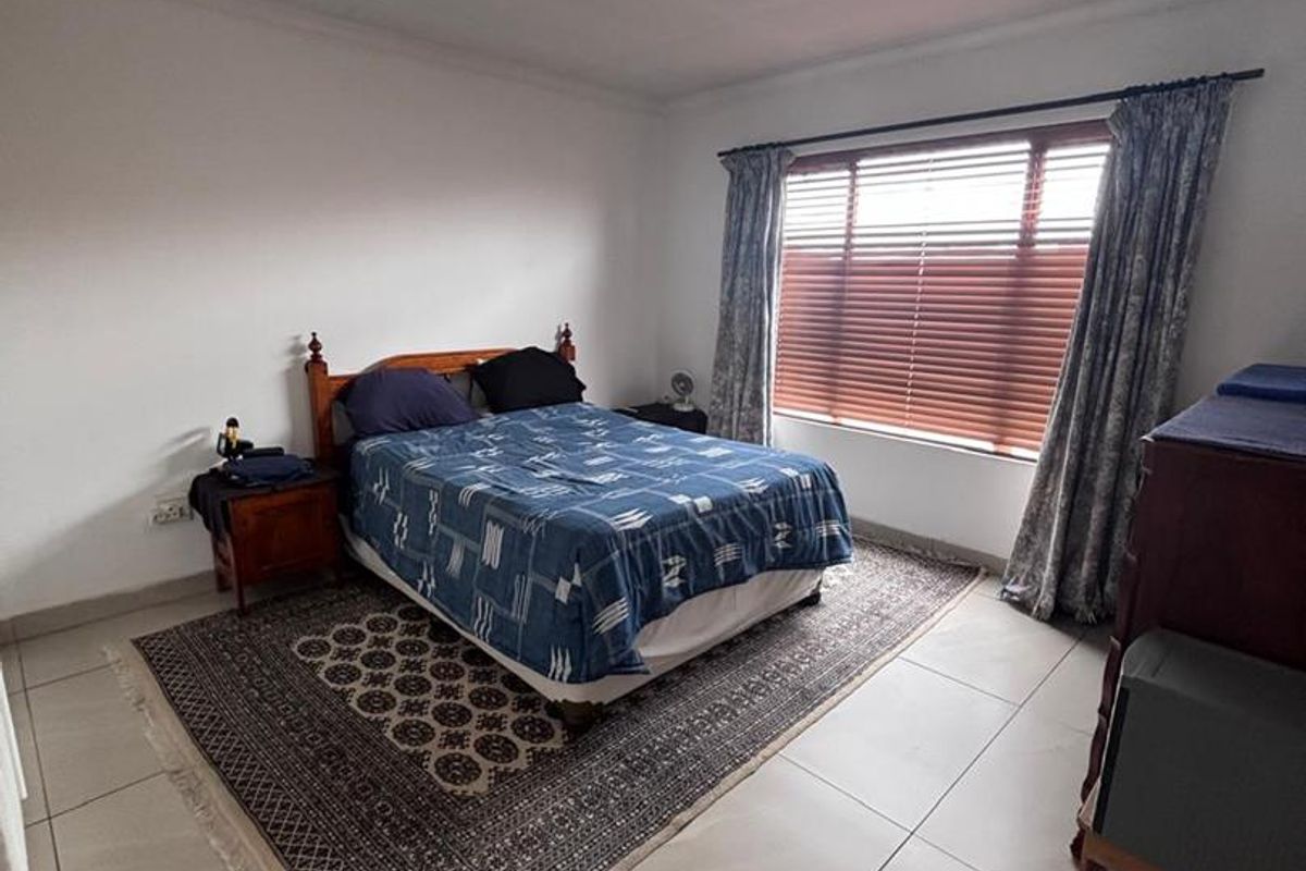 A well-lit bedroom featuring large format floor tiles, a window with fitted blinds, and a central ceiling light fixture.