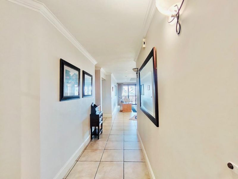 A well-lit hallway featuring neutral tiled flooring and crown molding, providing a clean transition between living spaces.