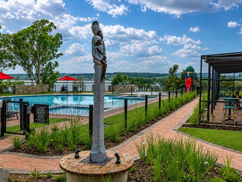 A well-maintained communal pool area featuring a swimming pool, water fountains, paved walkways, and landscaped gardens with scenic lake views.