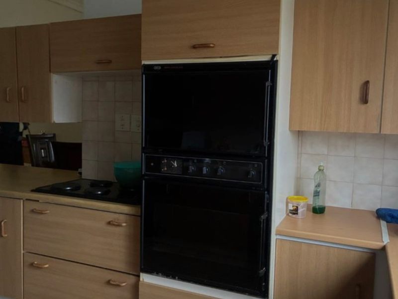A dated kitchen featuring wood-look laminate cabinetry, integrated oven, and tiled splashbacks, offering a functional layout ready for modern renovation.