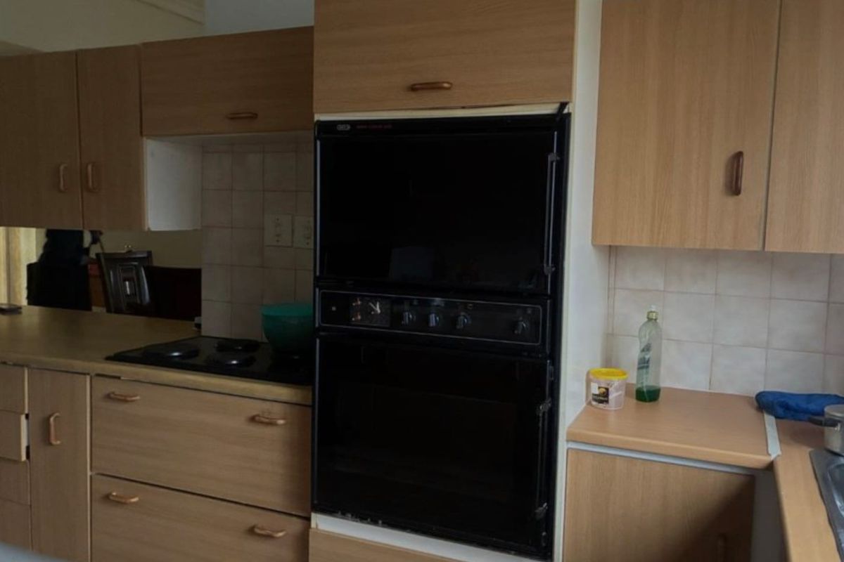 A dated kitchen featuring wood-look laminate cabinetry, integrated oven, and tiled splashbacks, offering a functional layout ready for modern renovation.