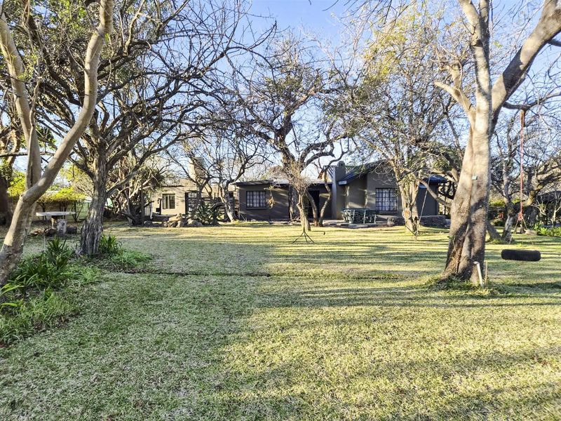 A spacious rear garden featuring mature trees and a view of the back elevation of the house.