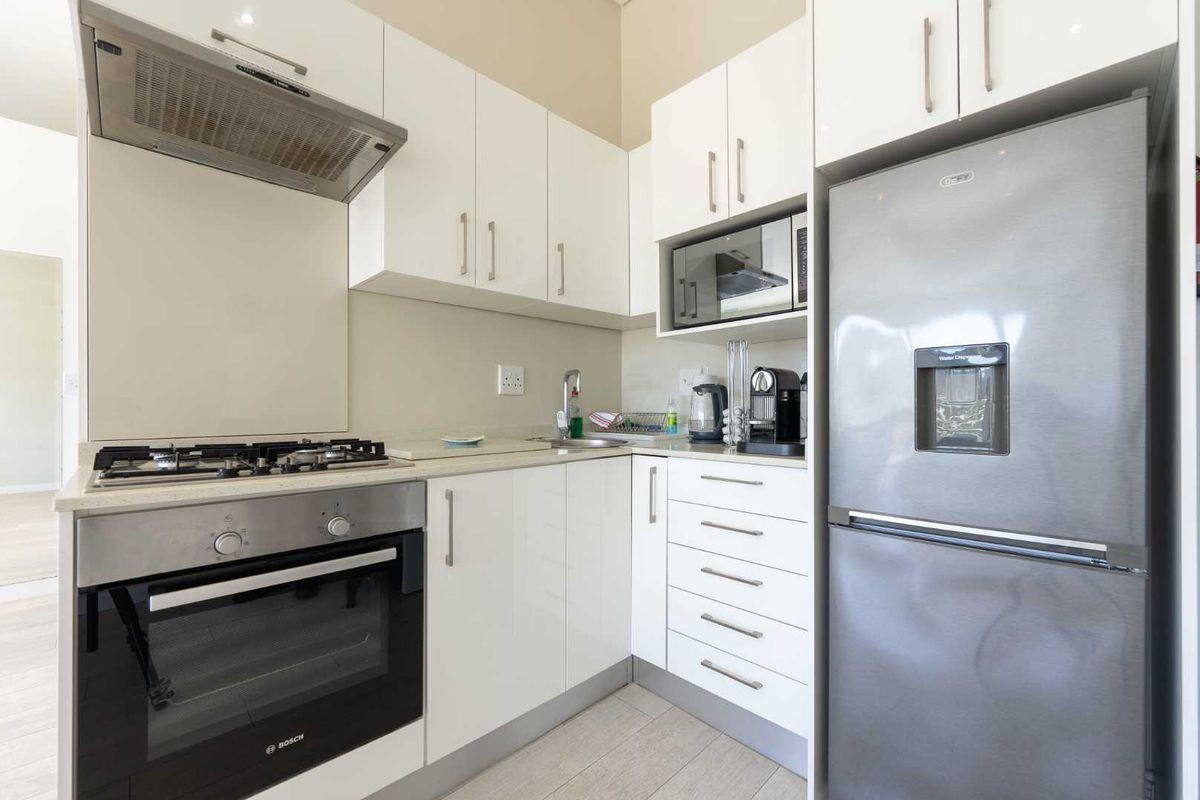 Modern kitchen featuring white gloss cabinetry, stone countertops, integrated gas hob, oven, extractor fan, and built-in microwave.