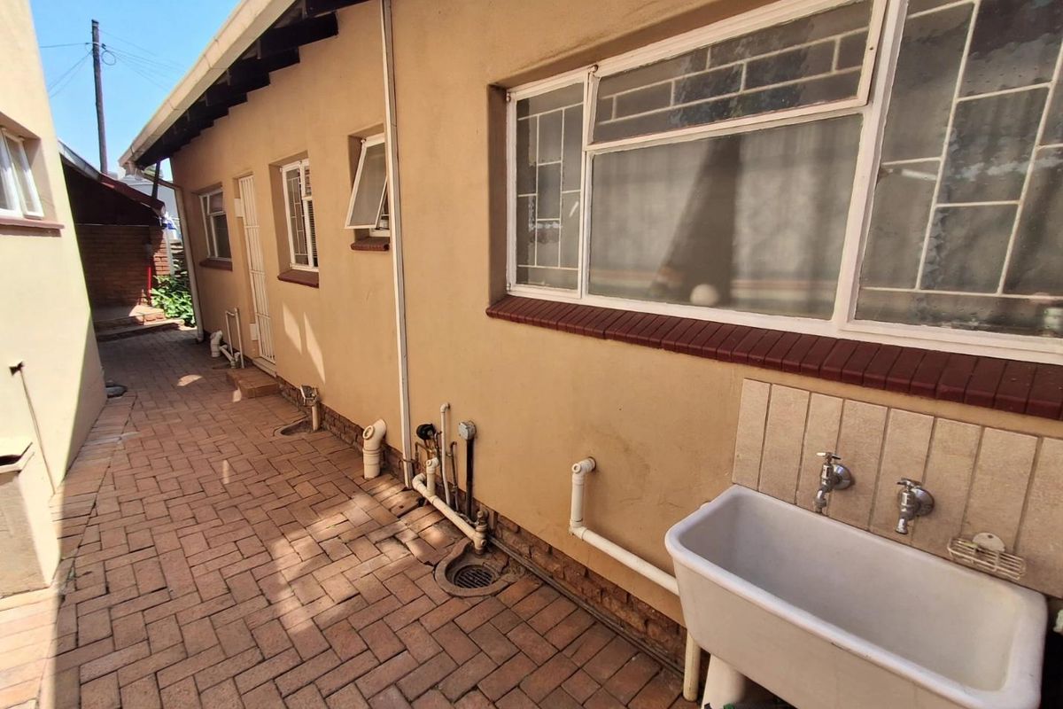 Rear exterior area featuring brick paving, an external utility sink, and exposed plumbing along the building facade.