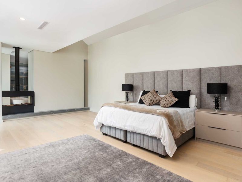 Spacious bedroom featuring light hardwood flooring, a vaulted ceiling, recessed lighting, and a modern built-in fireplace.
