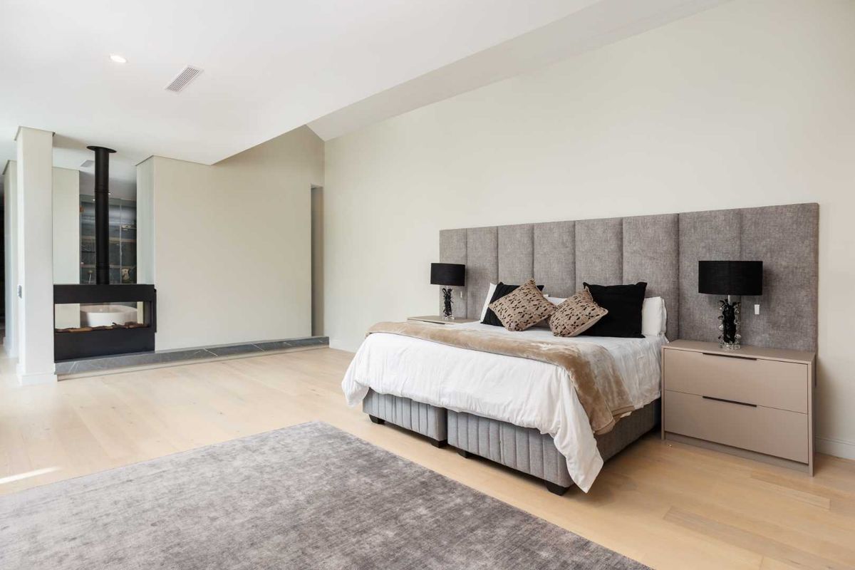 Spacious bedroom featuring light hardwood flooring, a vaulted ceiling, recessed lighting, and a modern built-in fireplace.