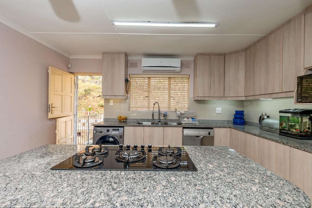 Modern kitchen featuring granite countertops, a built-in gas hob, ample cabinetry, and integrated appliances, with direct access to an outdoor area.