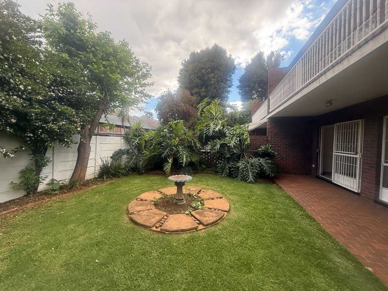 A private rear garden featuring a paved patio area, established landscaping, and a balcony overlooking the lawn.
