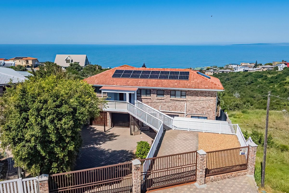 Aerial view of a multi-level brick house featuring a tiled roof with solar panels, a paved driveway, secure gated entrance, and ocean views.