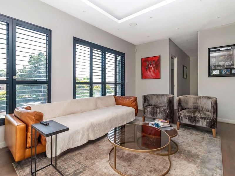 A modern, well-lit living room featuring hardwood flooring, recessed ceiling lighting, and black framed shutters providing natural light.