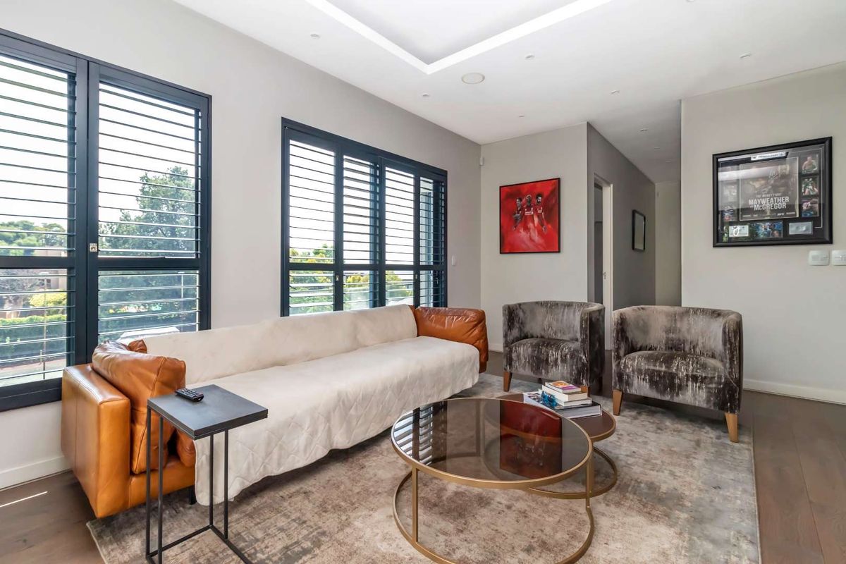 A modern, well-lit living room featuring hardwood flooring, recessed ceiling lighting, and black framed shutters providing natural light.