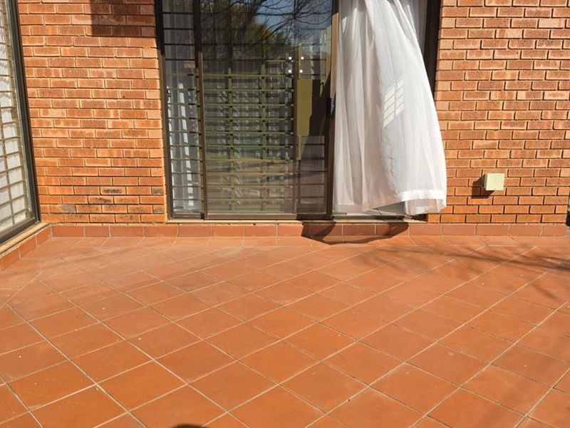 A private outdoor patio area featuring terracotta-style tiled flooring and direct access to the interior through a sliding glass door with security gate.