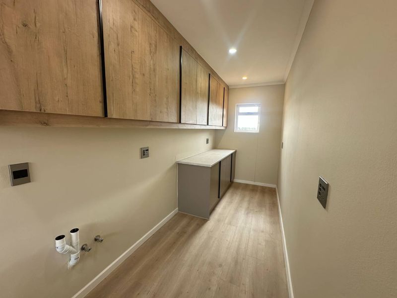 A clean, modern laundry room featuring extensive built-in cabinetry, laminate countertops, and dedicated plumbing connections for appliances.