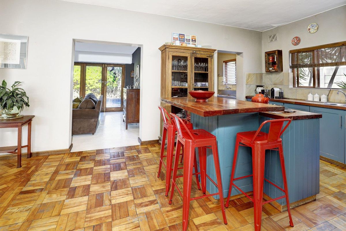 A kitchen featuring a central island with a wooden countertop, blue cabinetry, and parquet flooring, with an open-plan flow to the adjacent living area.