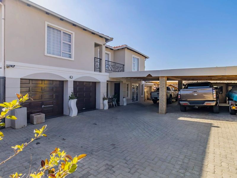 Front exterior view of the property featuring a paved driveway, double garage, and a covered carport area with an upper-level balcony.