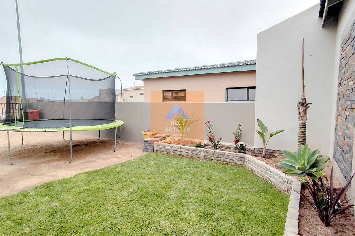 A private rear garden featuring a manicured lawn, a raised stone-clad garden bed, and a decorative stone feature wall.