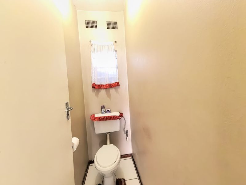 A compact guest toilet featuring tiled flooring and ventilation grilles, currently showing signs of wear and dated finishes.