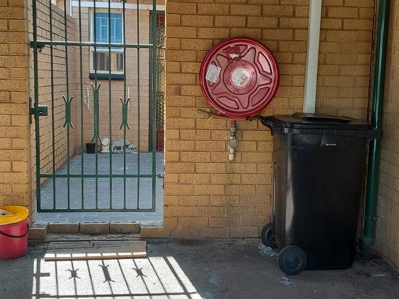 A functional utility area featuring a brick wall, metal gate, and a mounted fire hose reel under a corrugated metal roof.