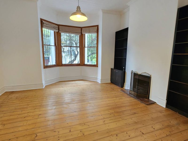 A bright living room featuring polished timber flooring, a classic bay window, built-in shelving, and a fireplace.